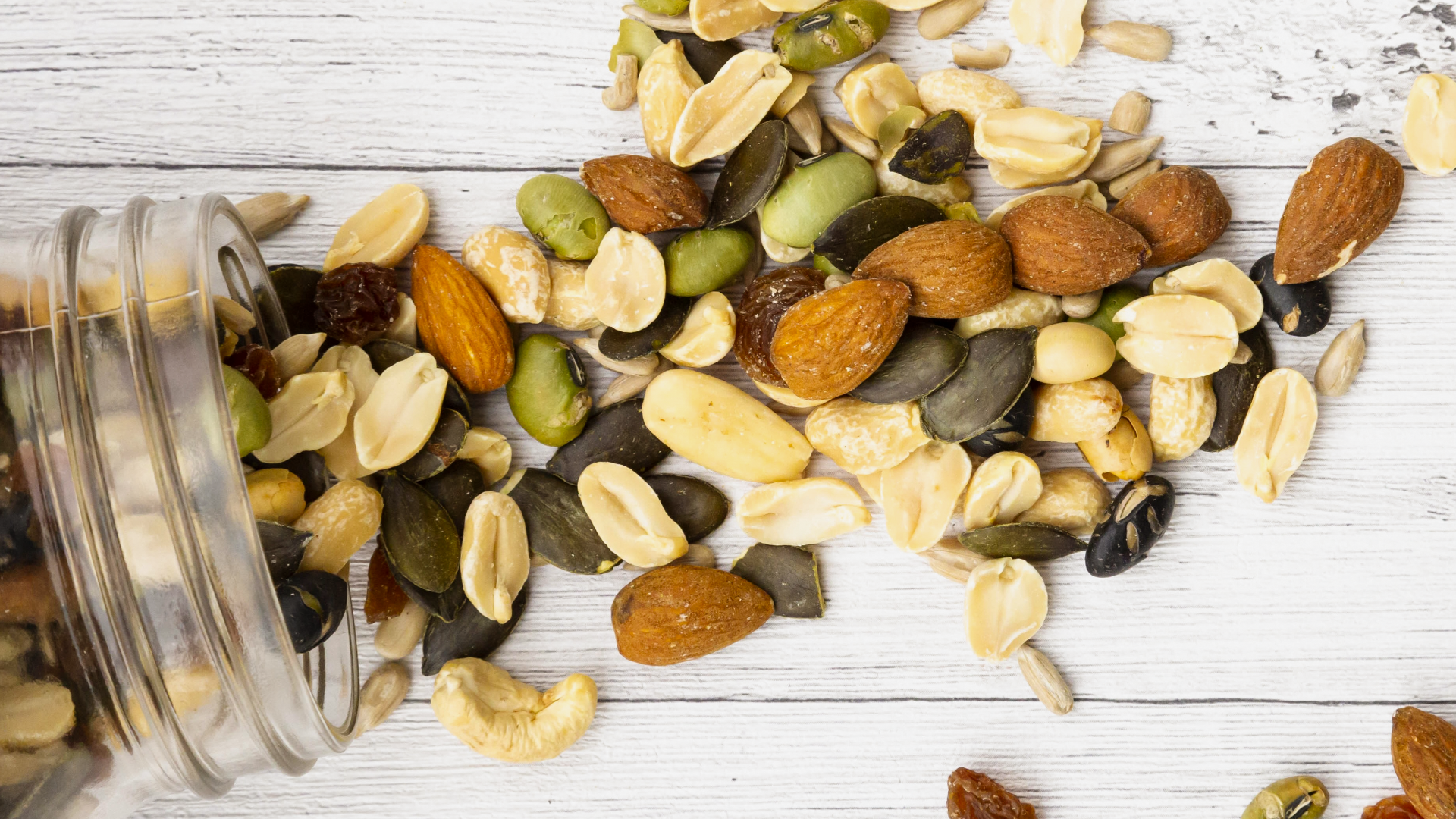Nüsse und Samen laufen aus einem Glas auf Tisch.