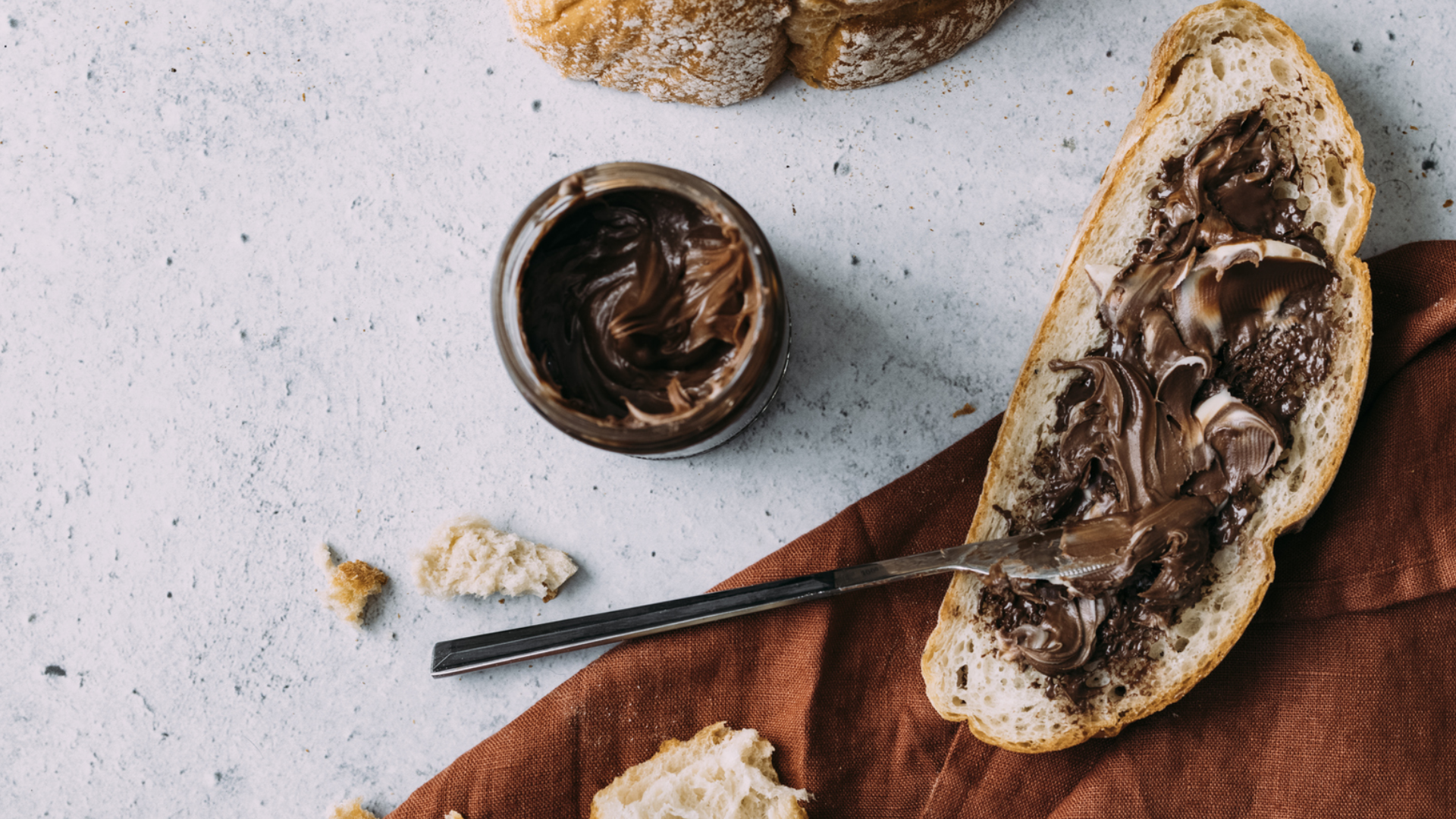 Brotscheibe mit Nuss-Nougat-Creme, Glas und Messer.
