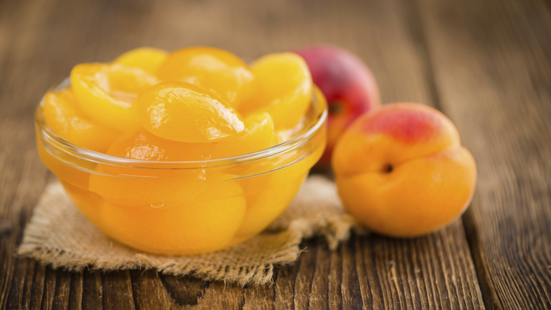 Aprikosenhälften in Schale neben frischen Aprikosen auf Holz.