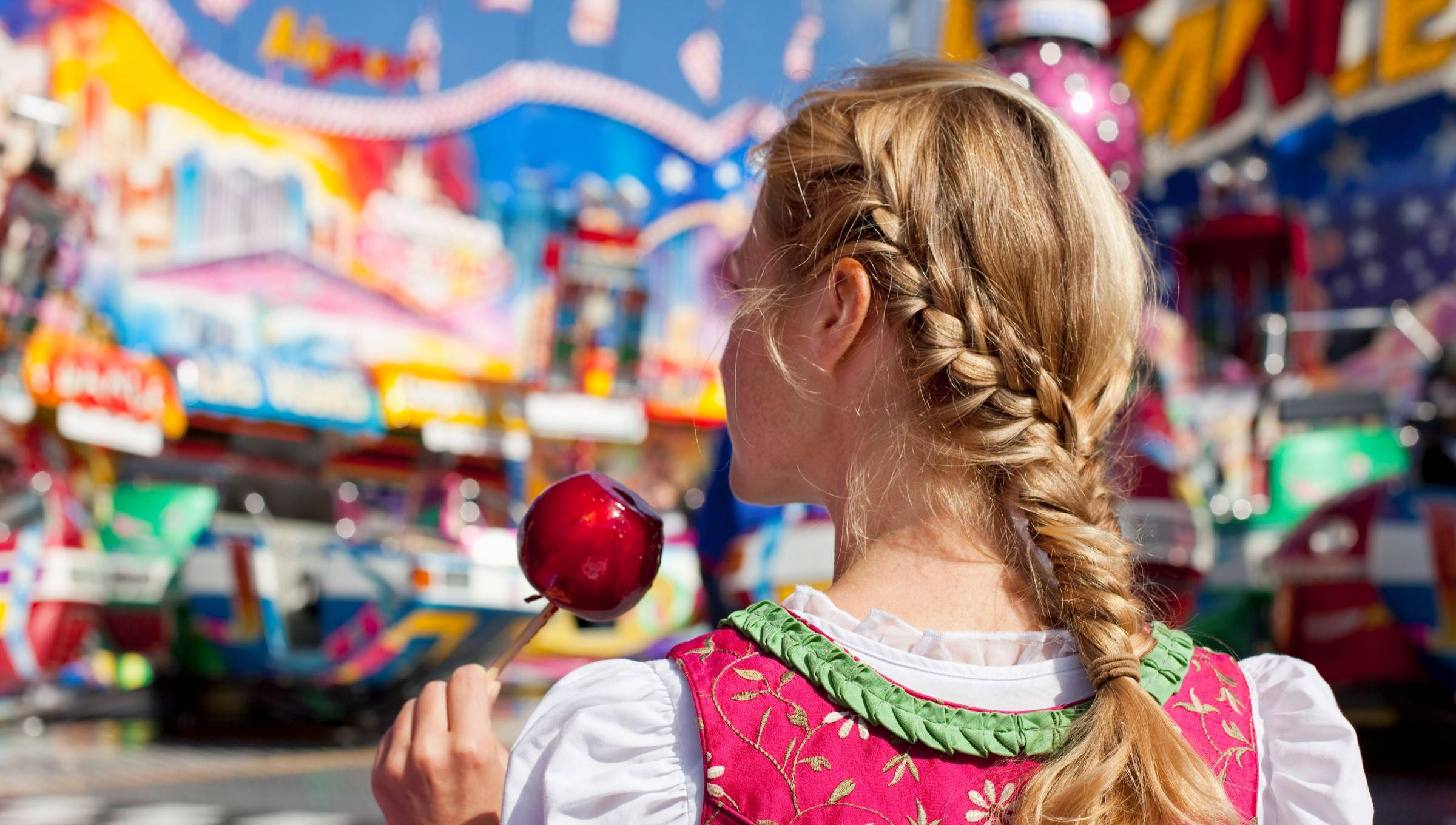 Eine Frau im Dirndl genießt auf dem Oktoberfest einen kandierten Apfel.