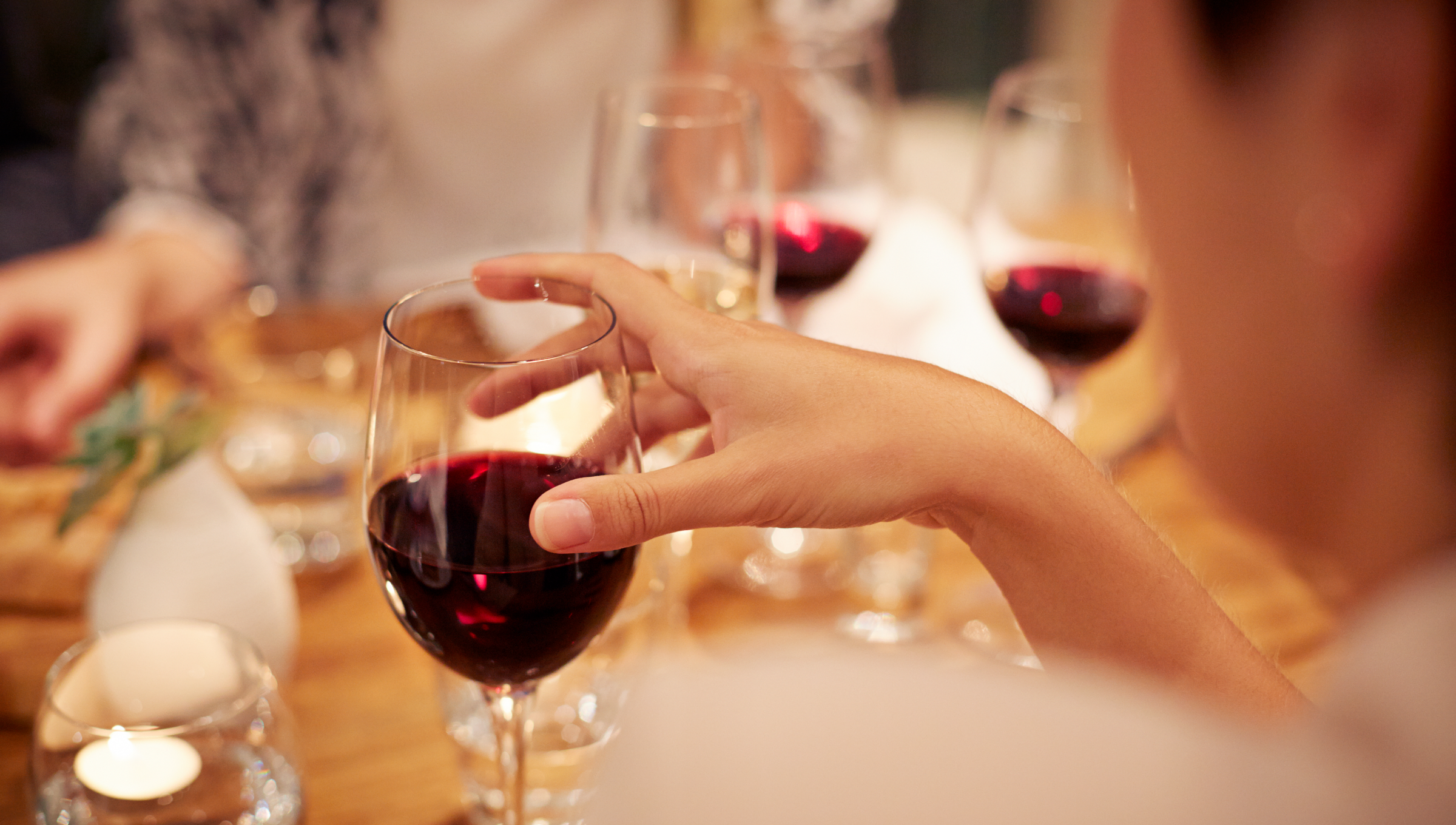 Menschen sitzen an einem Tisch und trinken Rotwein.