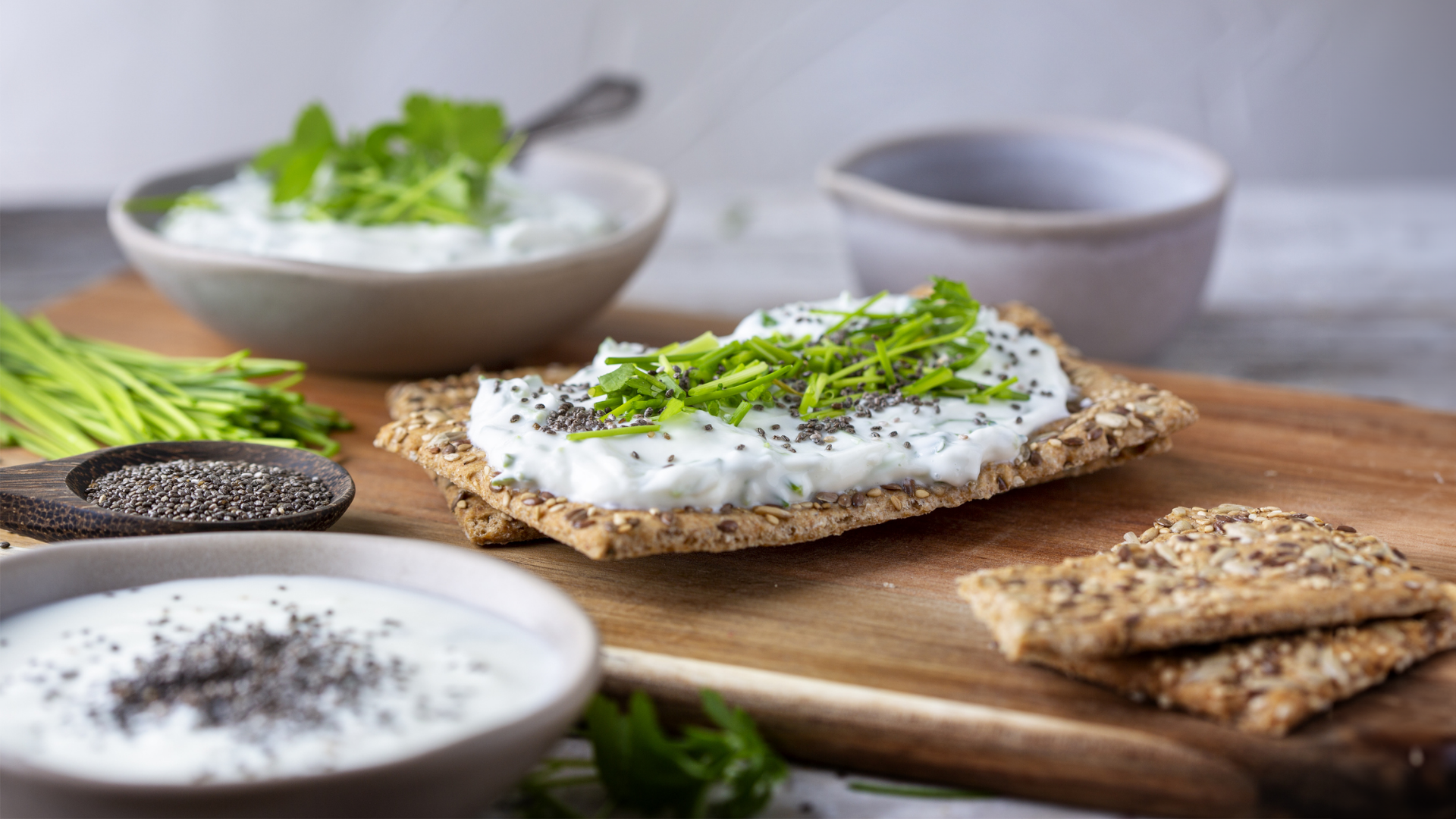Knäckebrot mit Quark, Schnittlauch und Chiasamen auf Holzbrett.