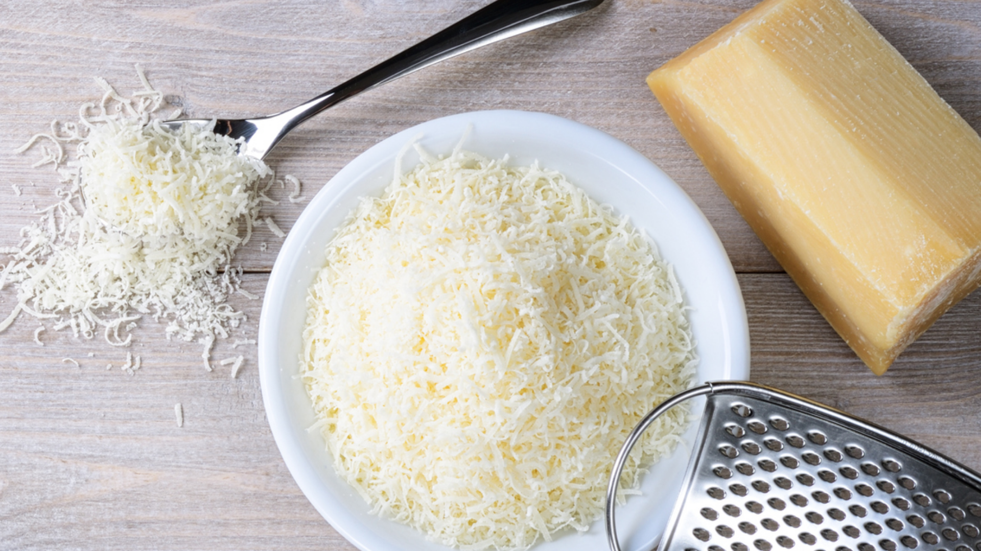 Geriebener Käse, Käsestück, Reibe und Löffel auf Holz.