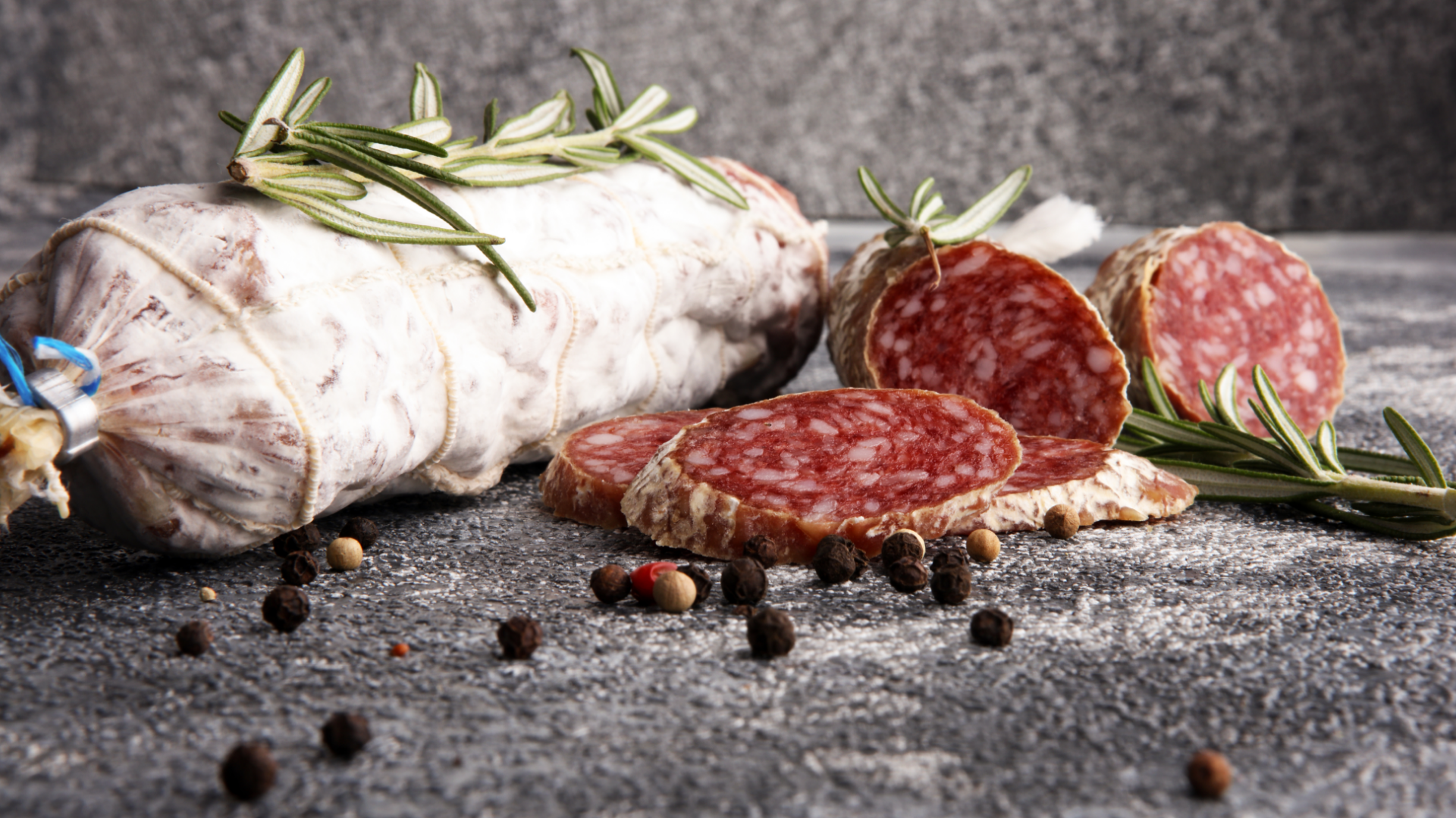 Salami, ganz und geschnitten, mit Rosmarin und Pfefferkörnern.