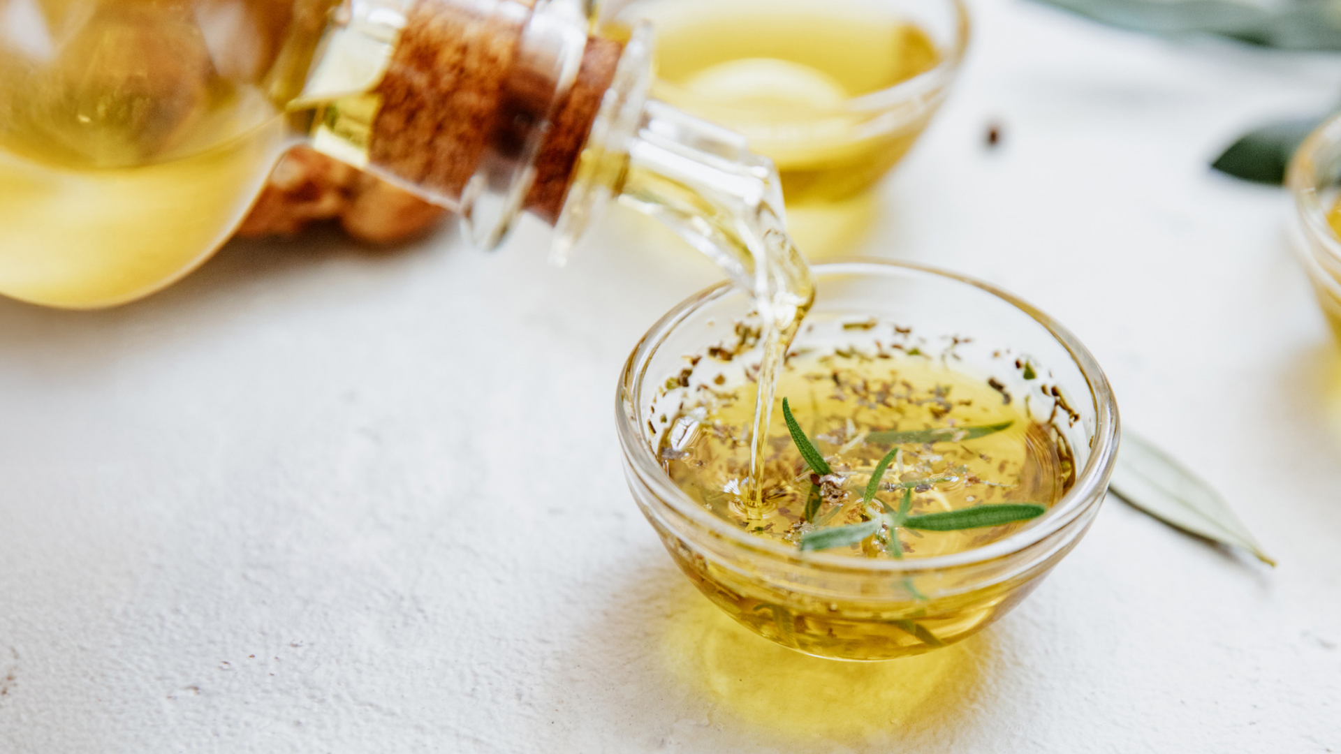 Klares Öl mit Kräutern wird in Glasschale gegossen.