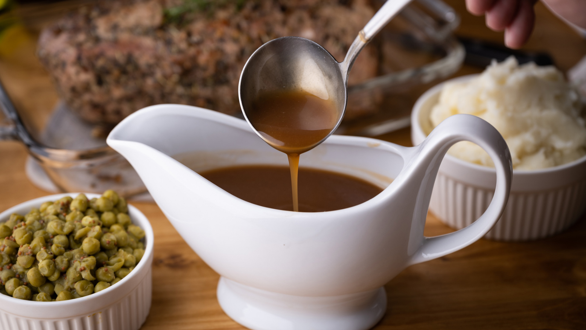 Bratensoße wird mit Schöpflöffel in Soßenboot gegossen.