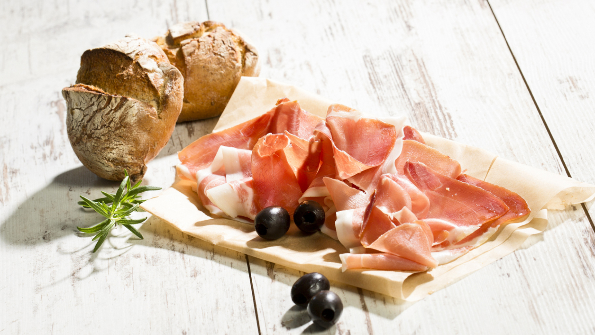 Roher Schinken, Brötchen, Oliven und Rosmarin auf Holz.