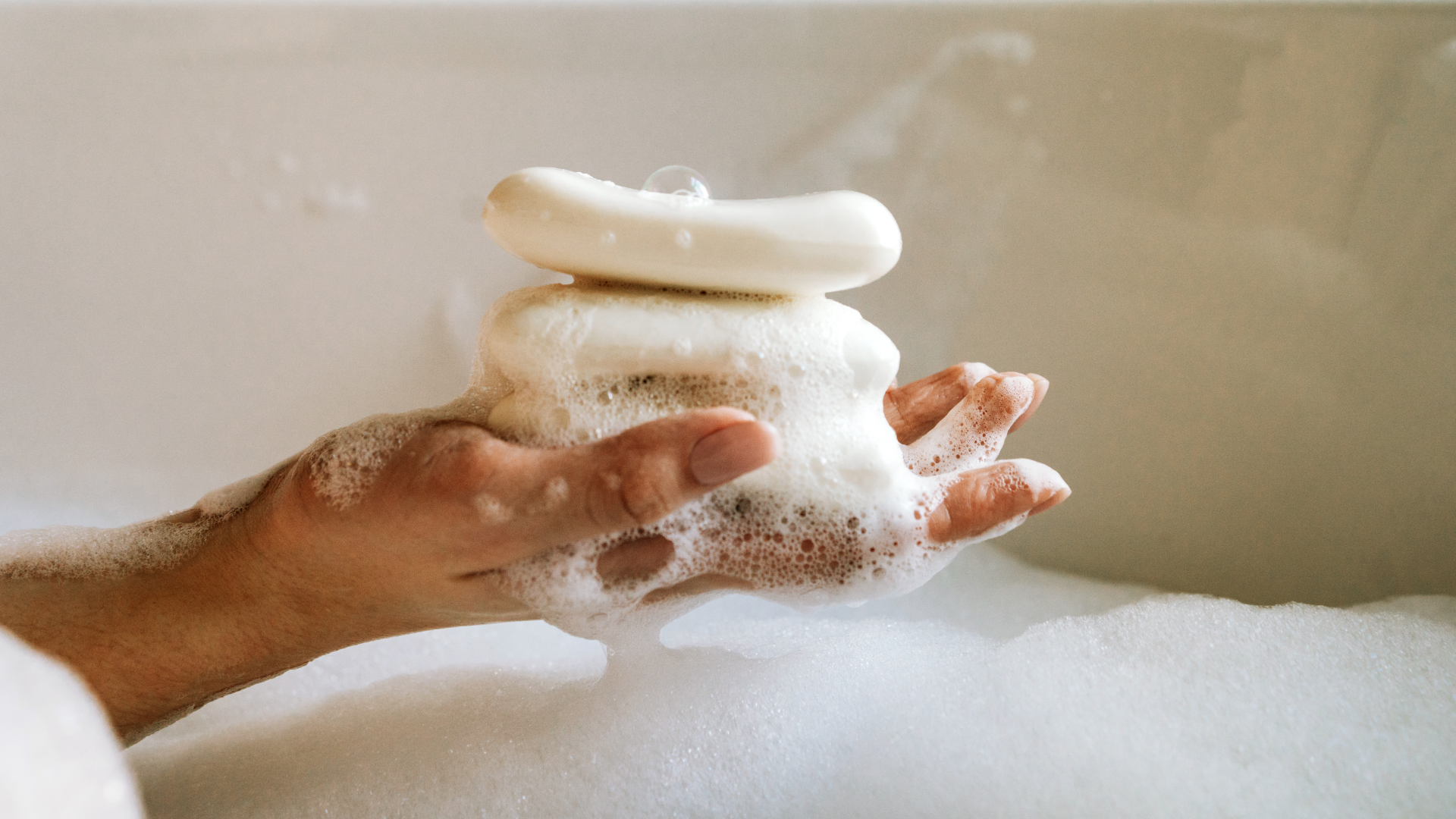 Hand hält schäumende Seife in Badewanne.