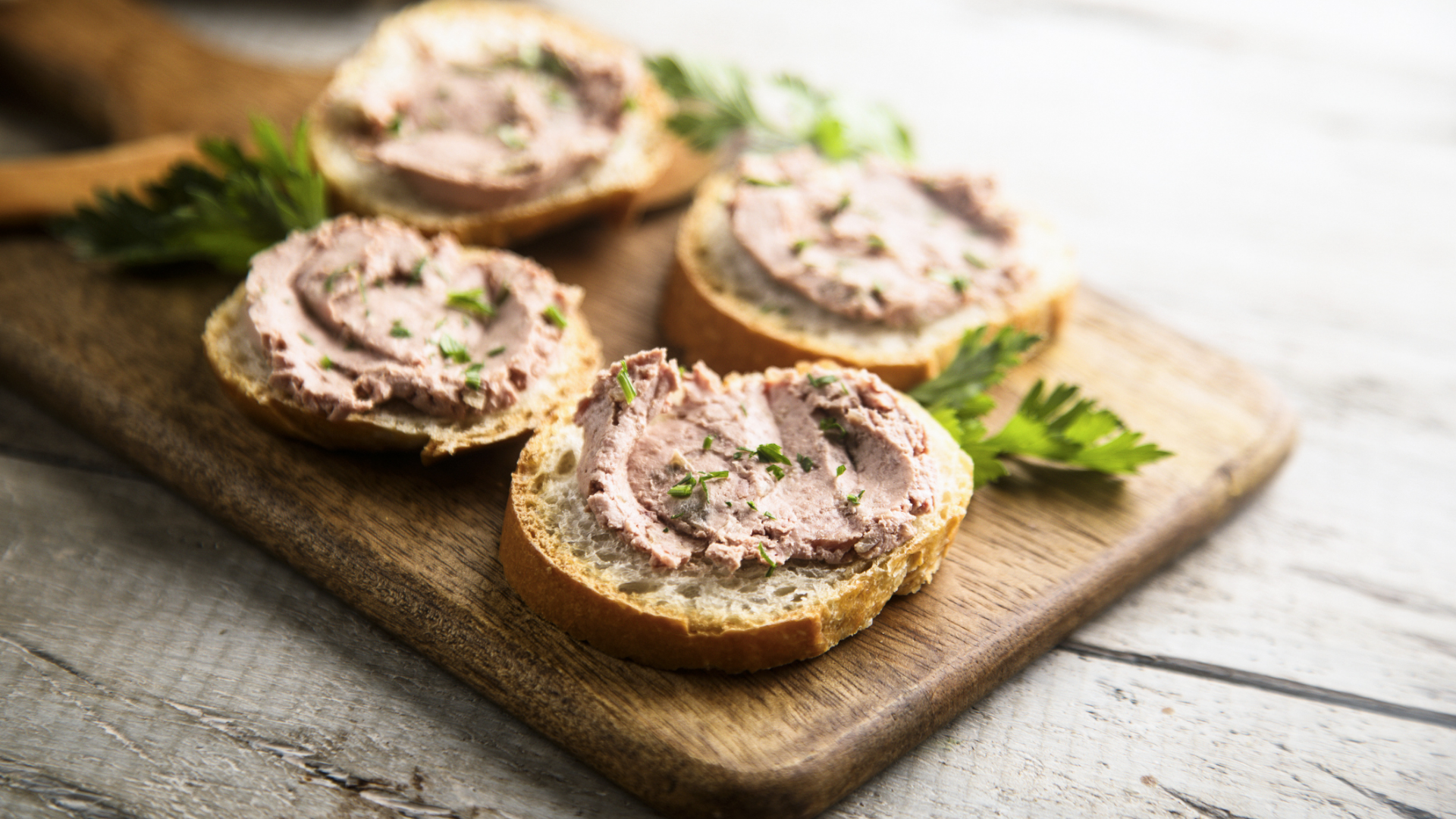 Vier Brotscheiben mit Streichwurst und Kräutern auf Holzbrett.