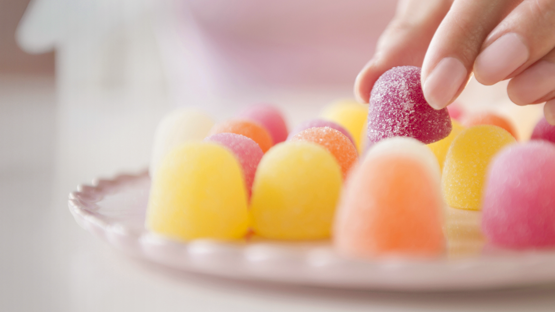 Zuckerbestreute Geleebonbons auf Teller, Hand nimmt eines.