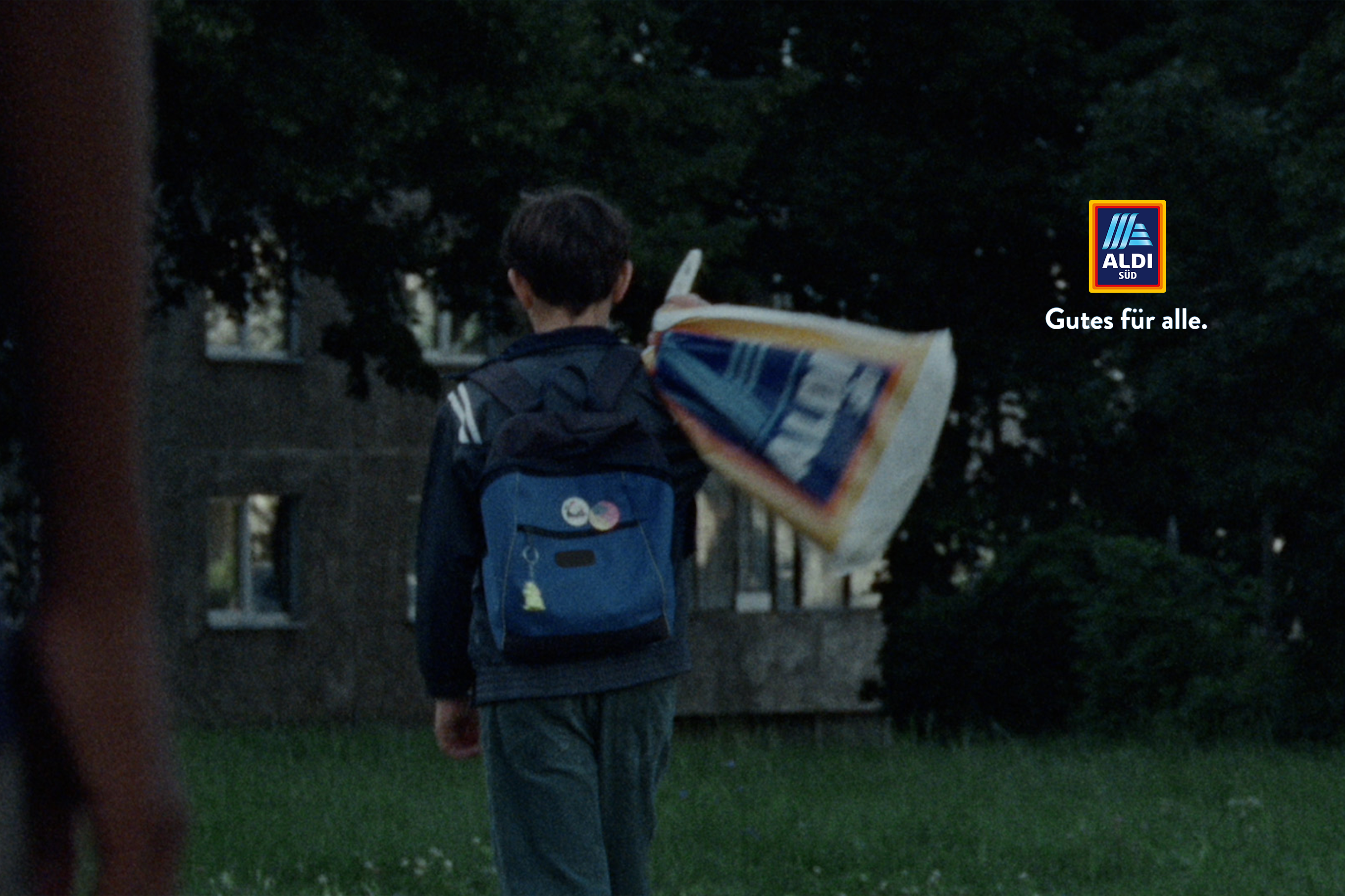 Junge mit Schulrucksack und Aldi-Einkaufstüte in einem Wohnviertel.