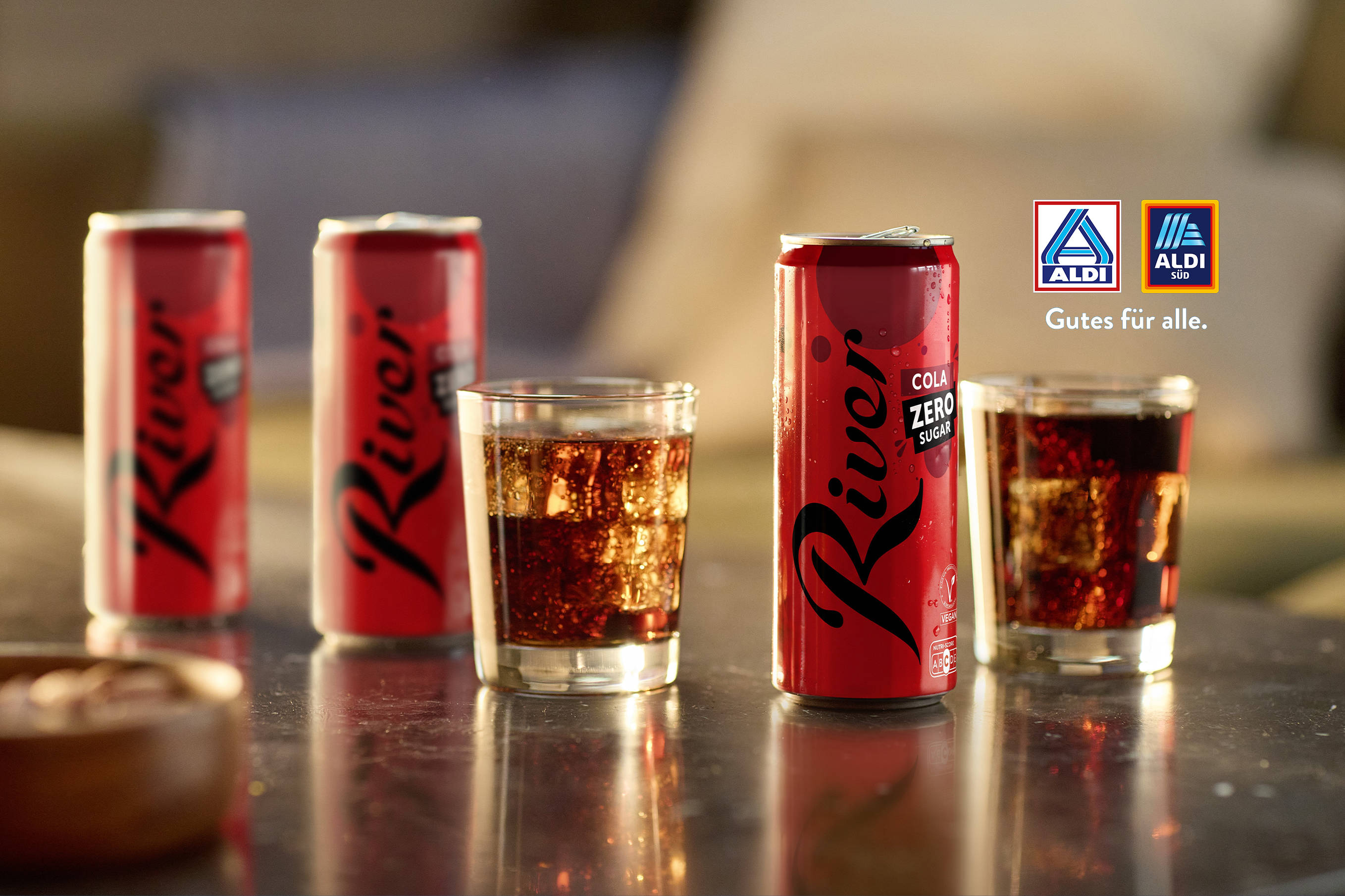 Auf einem Tisch stehen 3 ALDI River Cola Dosen und 2 Gläser gefüllt mit Cola.