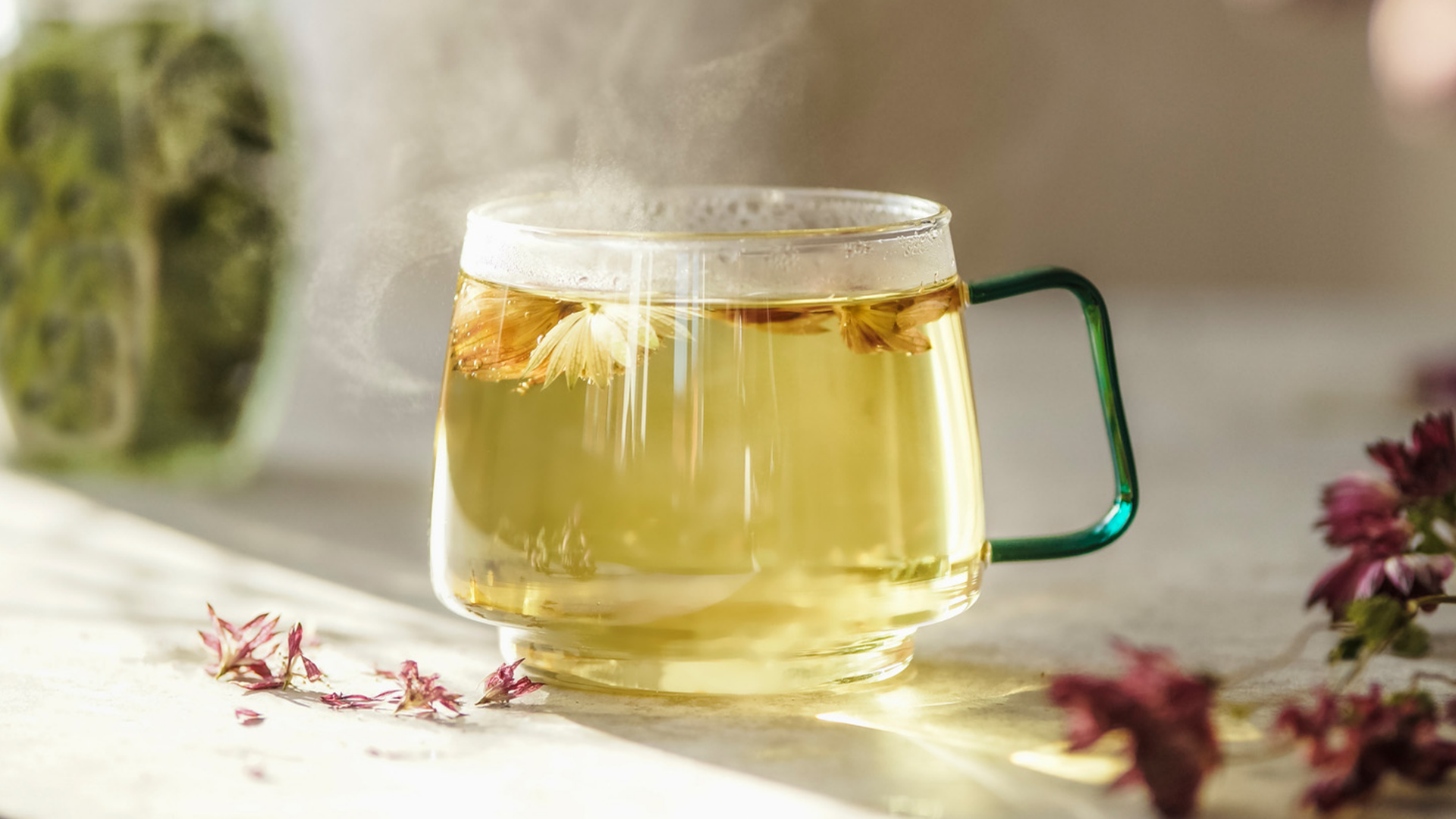 Dampfender Kräutertee in Glasbecher mit Blumen.