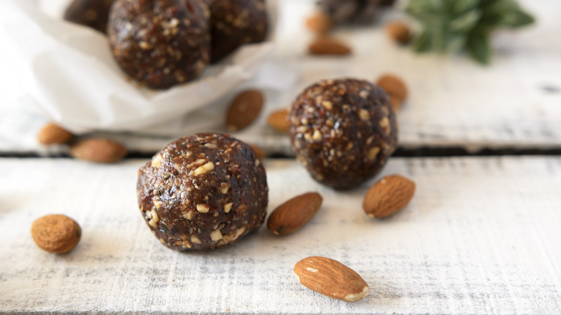Dunkle Nussbällchen und Mandeln auf hellem Holztisch.