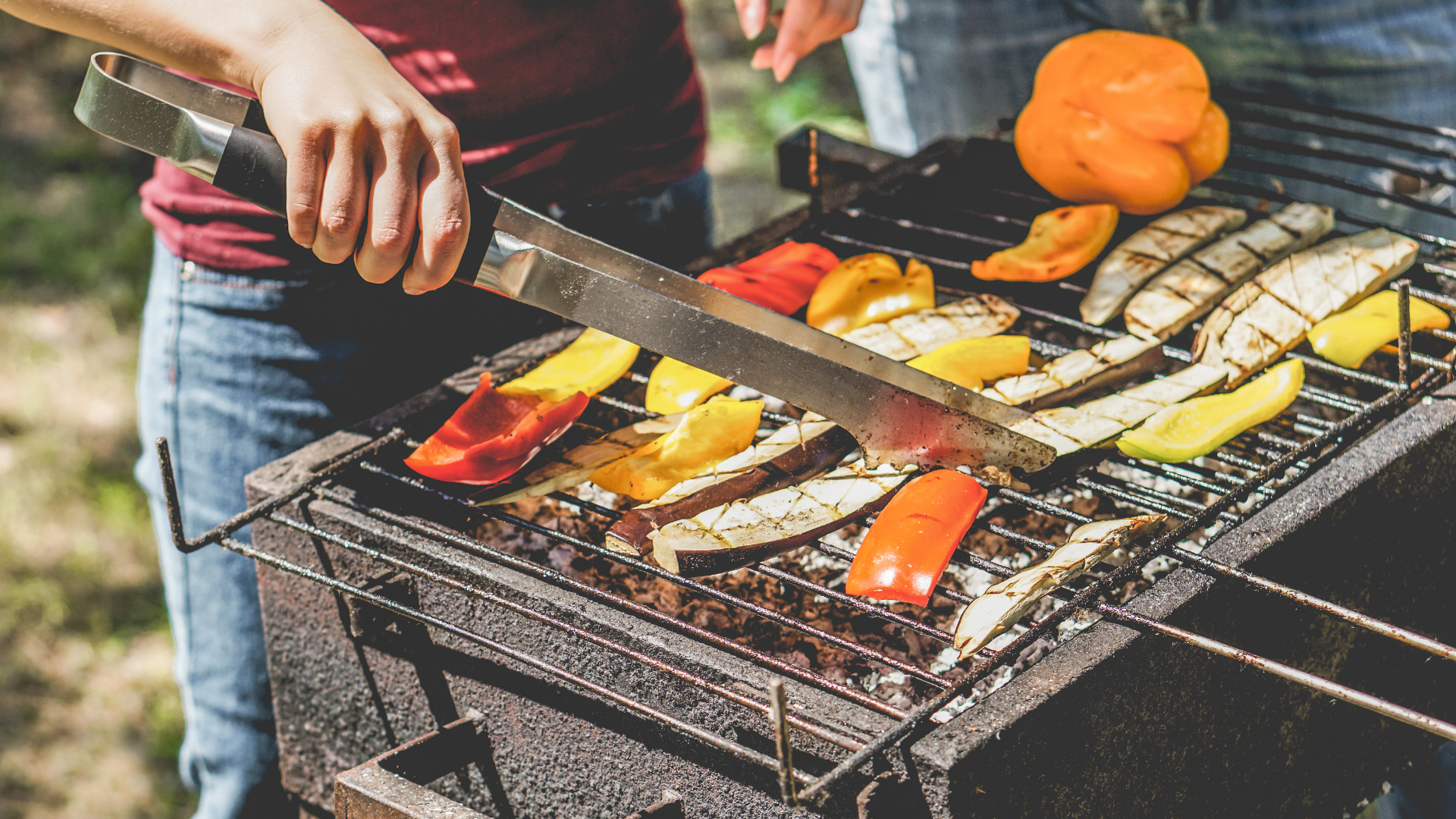 Gemüse wird auf einem Grill mit einer Zange gewendet.
