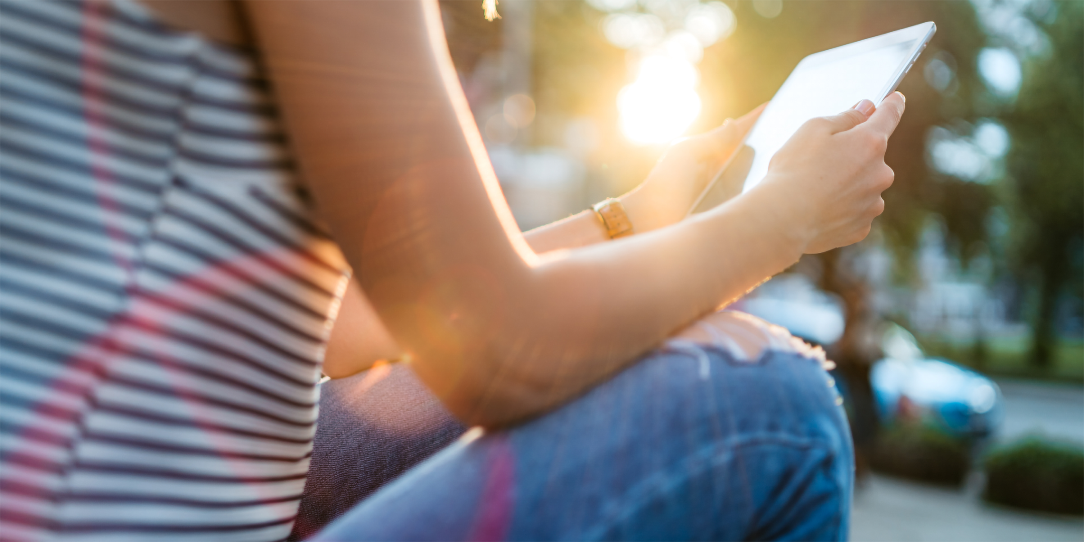 Person sitzt im Freien und benutzt ein Tablet bei Sonnenlicht.