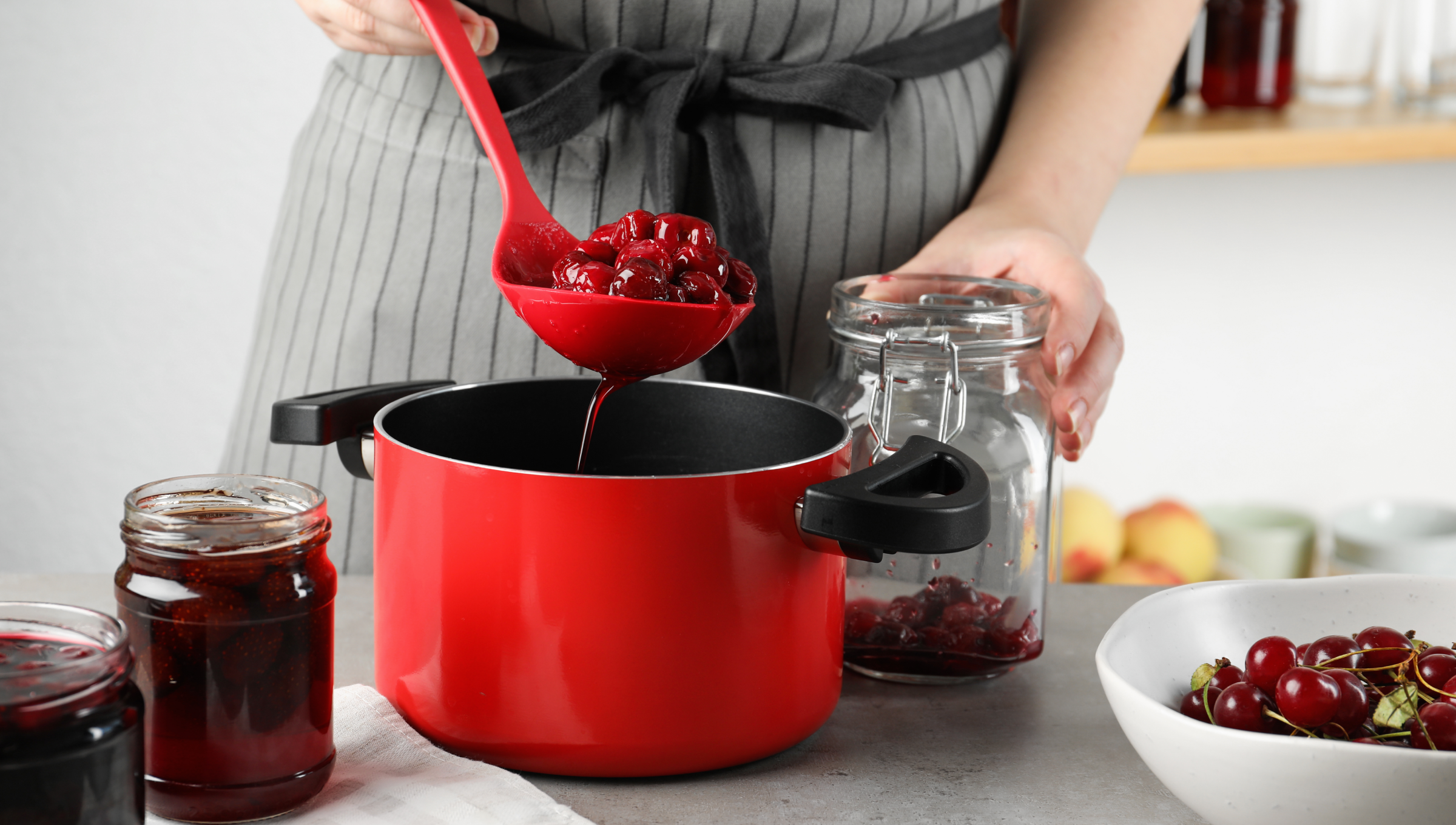 Person füllt Kirschkompott mit einer Kelle in ein Glas zur Vorbereitung für das Einkochen im Backofen.