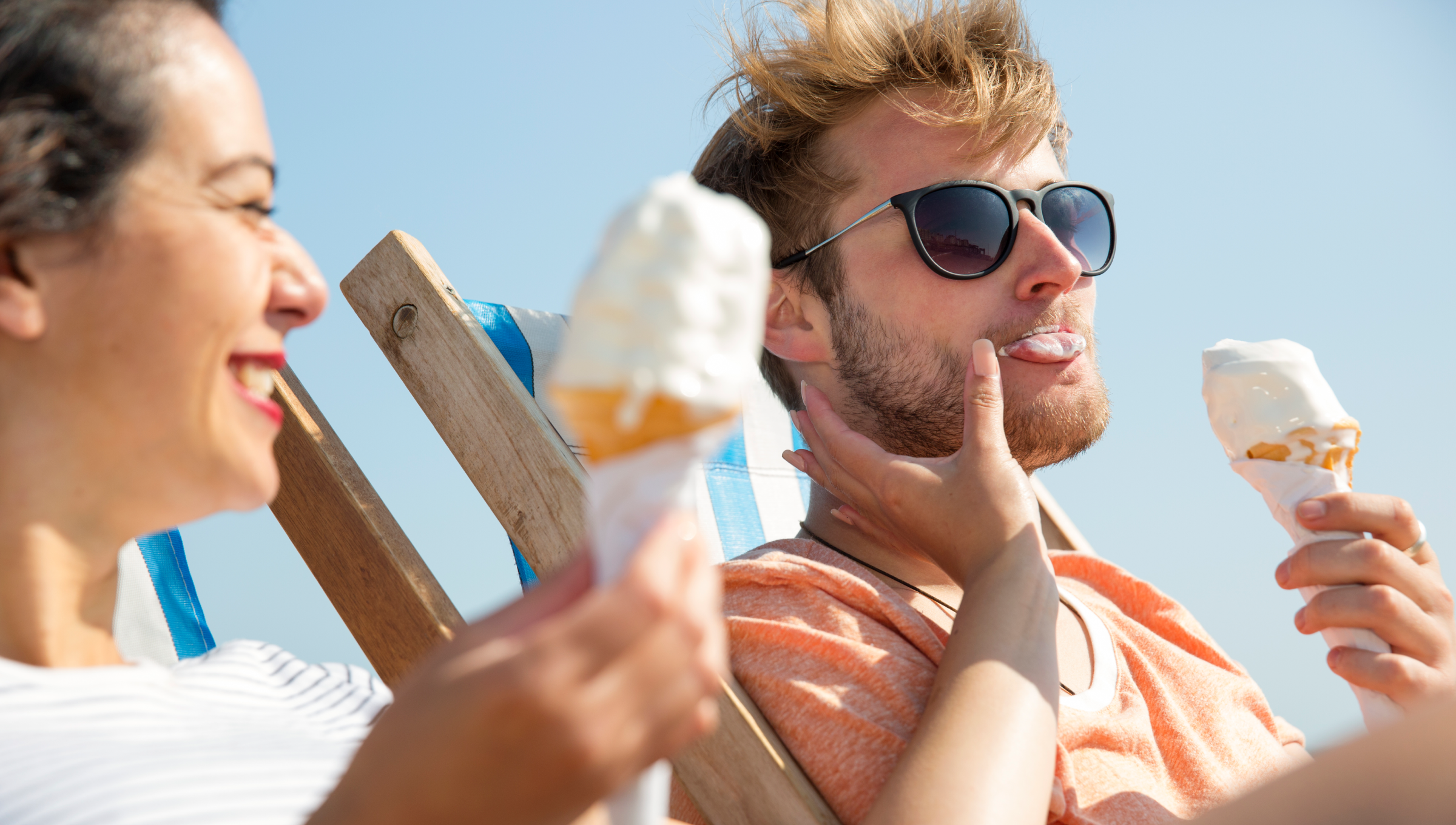 Ein Mann und eine Frau genießen ihr Eis in Liegenstühlen bei Sonnenschein unter blauem Himmel.