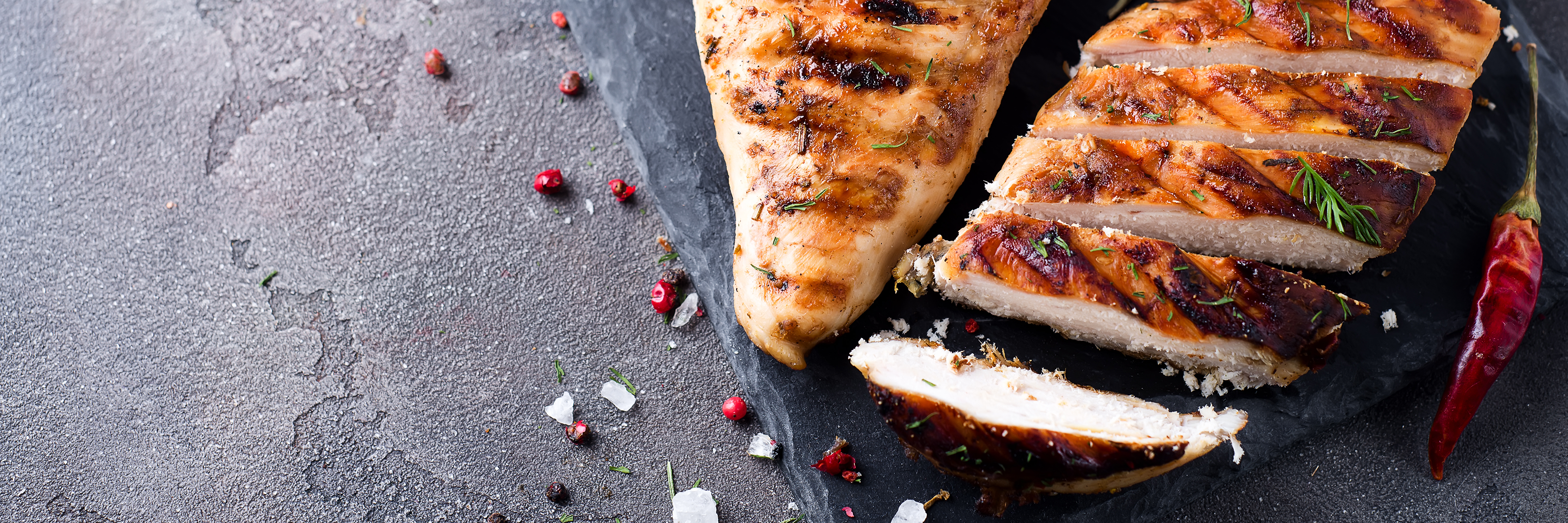 Rohe Hähnchenbrustfilets mit Petersilie auf einem Teller.