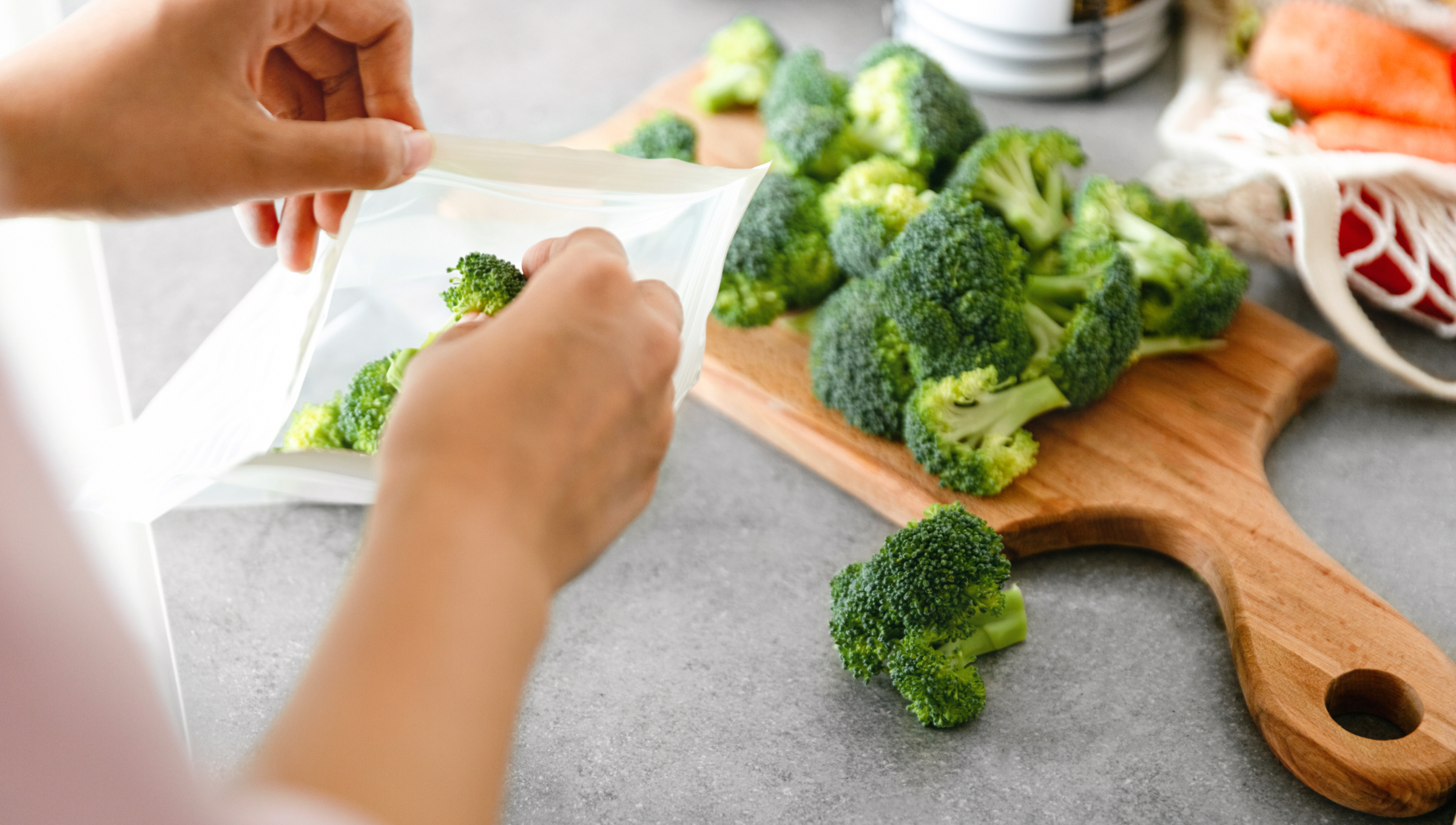 Person legt Brokkoliröschen, die auf einem Holbrett liegen in einen Gefrierbeutel.
