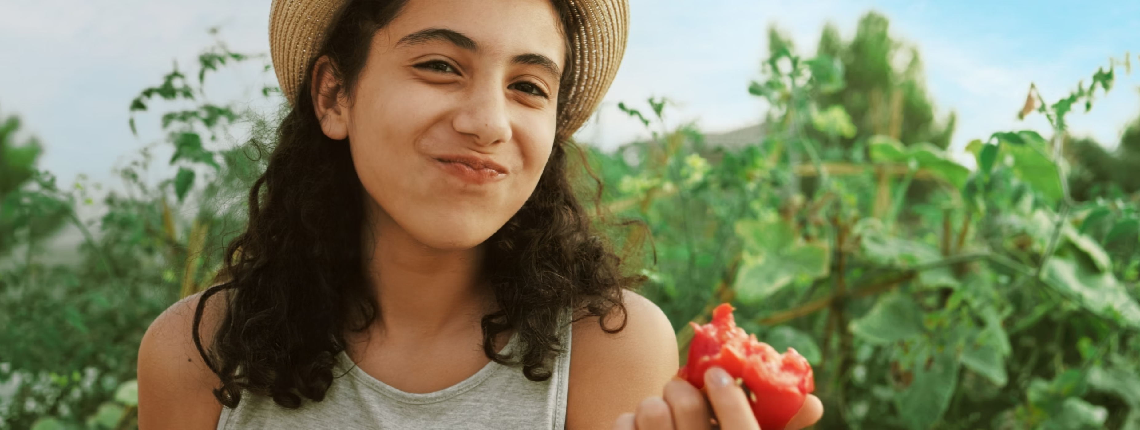 Mädchen mit Strohhut isst rote Frucht im Garten.