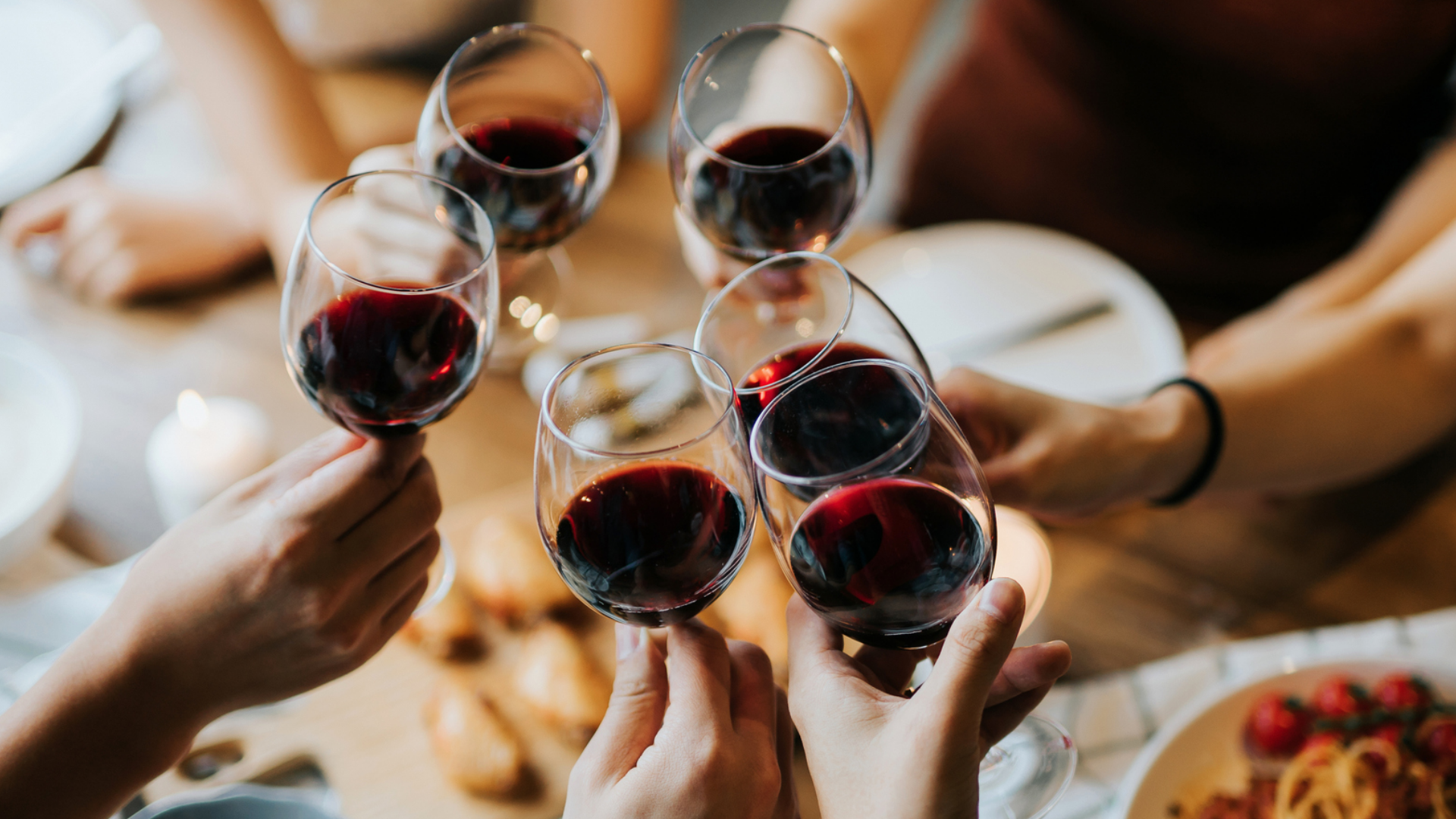 Anstoßen mit Rotwein bei Tisch, Essen im Hintergrund