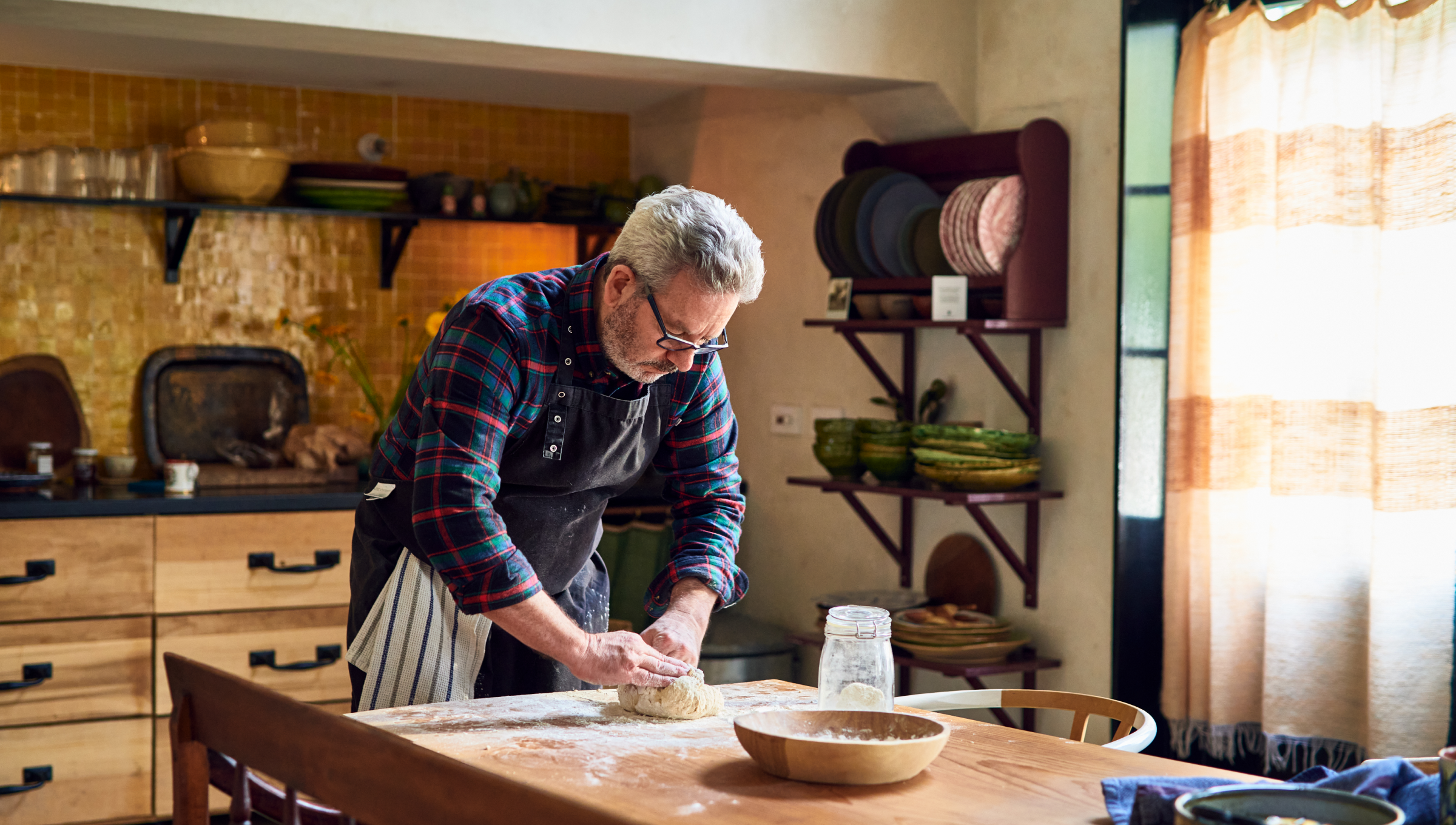 Mann knetet Sauerteig auf einem bemehlten Holztisch in der Küche.