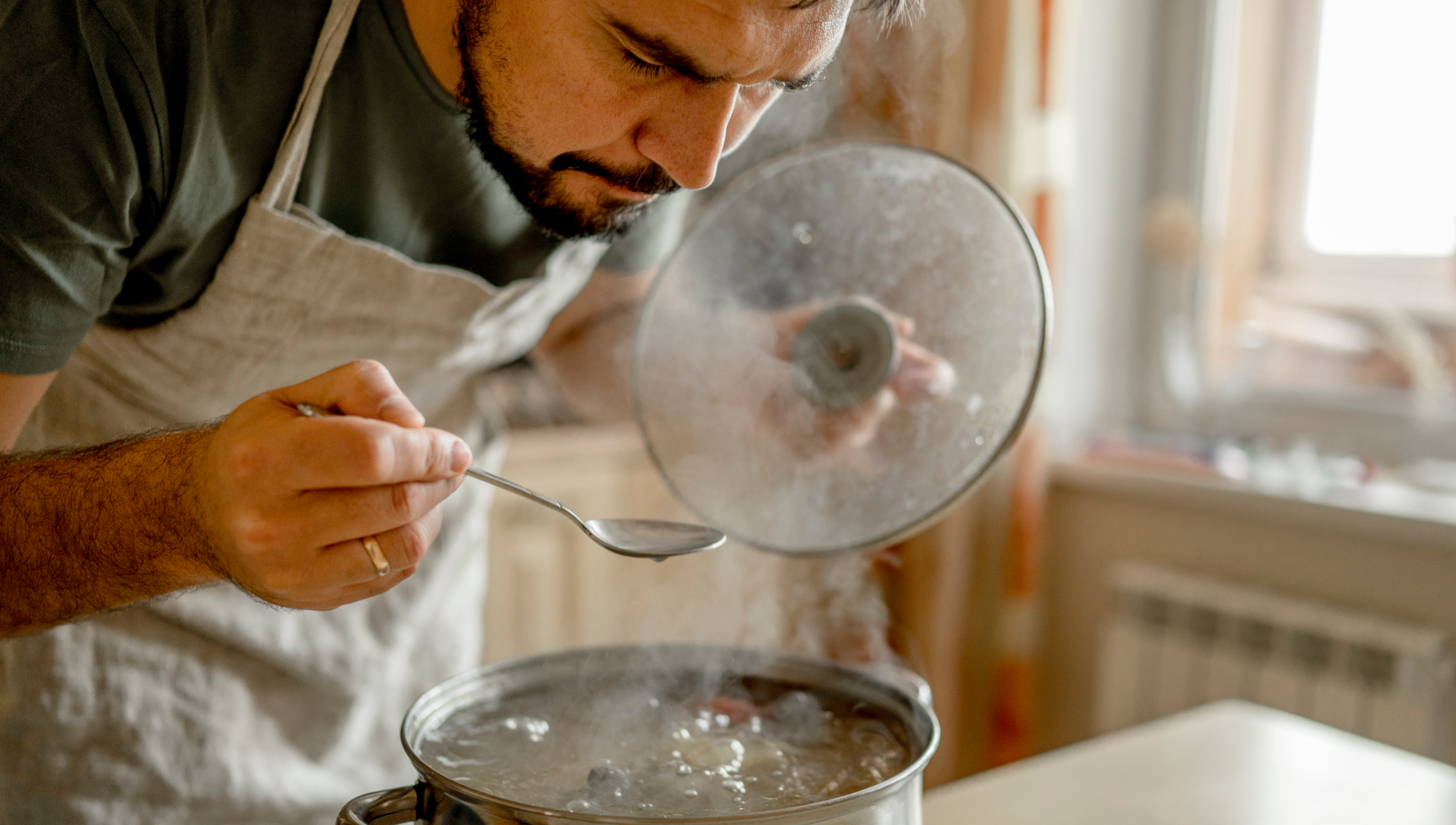 Mann probiert dampfendes Essen mit Löffel aus Topf.