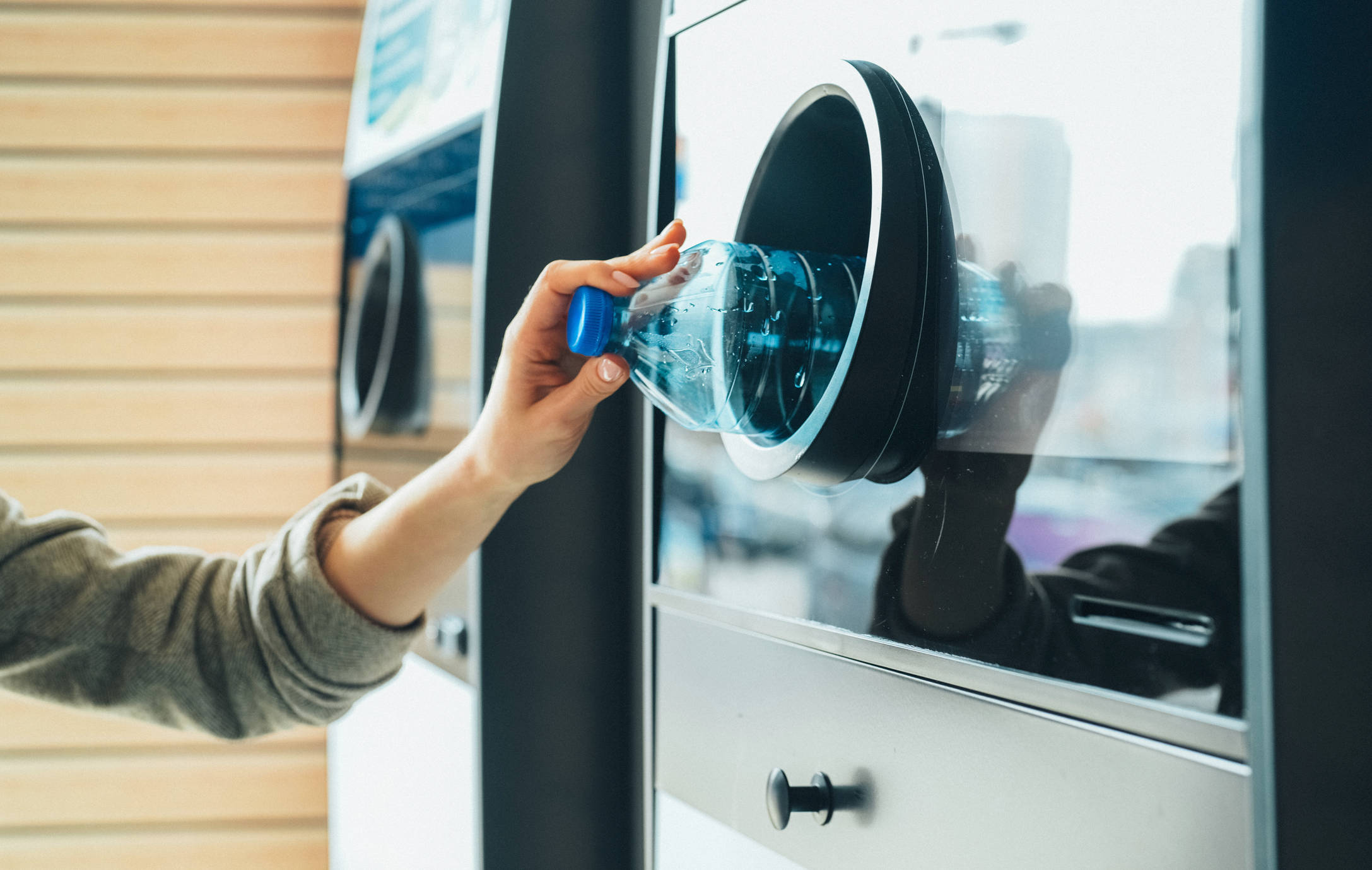 Person gibt eine leere PET Flasche in einen Pflandautomat.