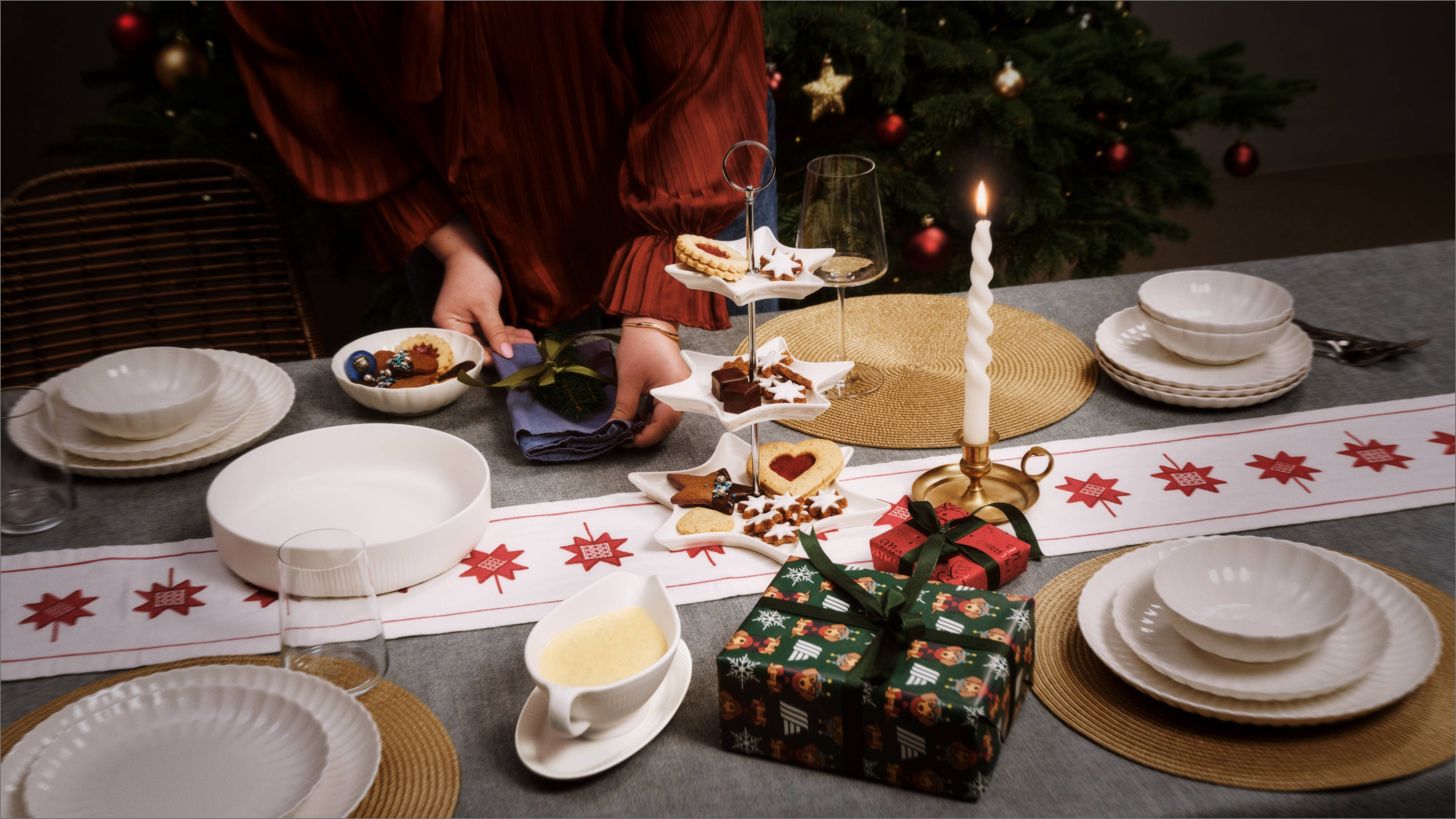 Eine Frau deckt einen weihnachtlich dekorierten Tisch ein.