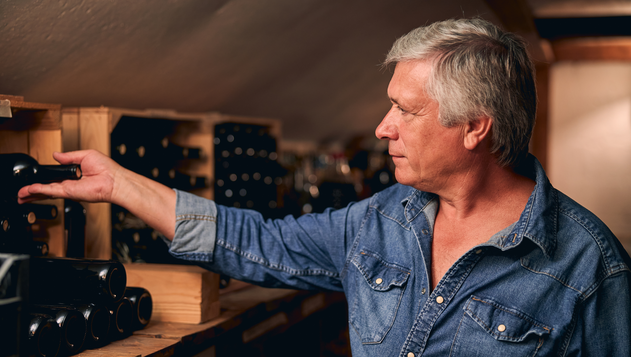 Mann legt eine Weinflasche zum Lagern in ein Weinregal.