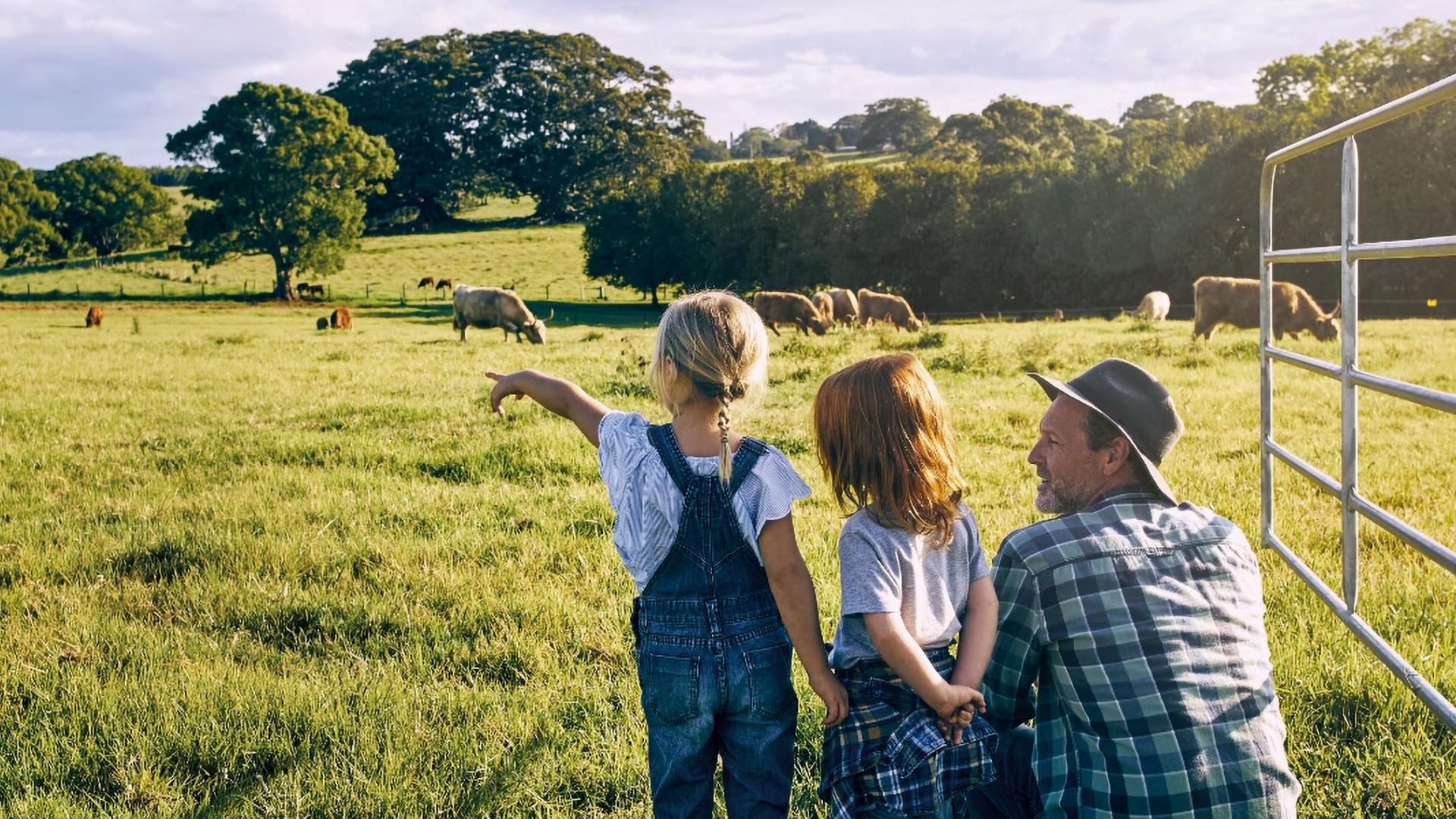 Ein Landwirt zeigt seinen Kindern Kühe auf einer Wiese.