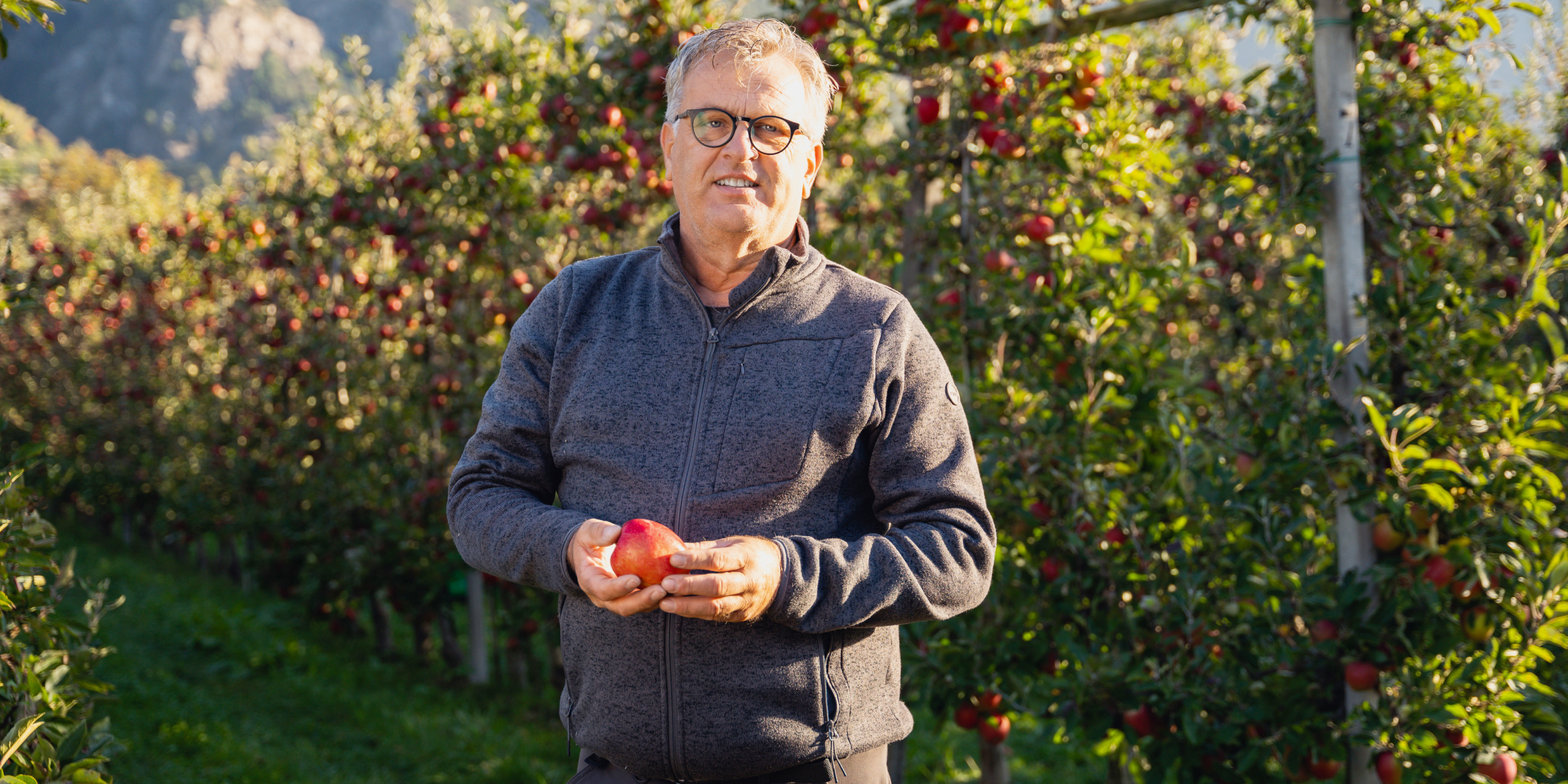 Biolandwirt Paul Wellenzohn hält einen reifen roten Apfel in einem üppigen Obstgarten